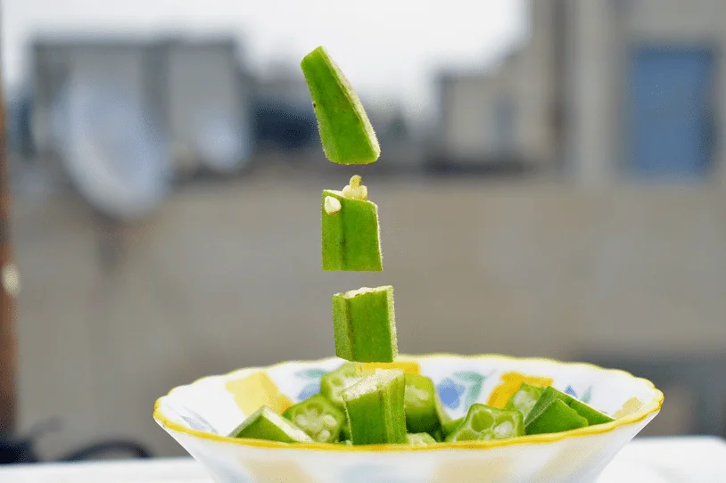 Sliced okra pieces falling into a bowl of okra