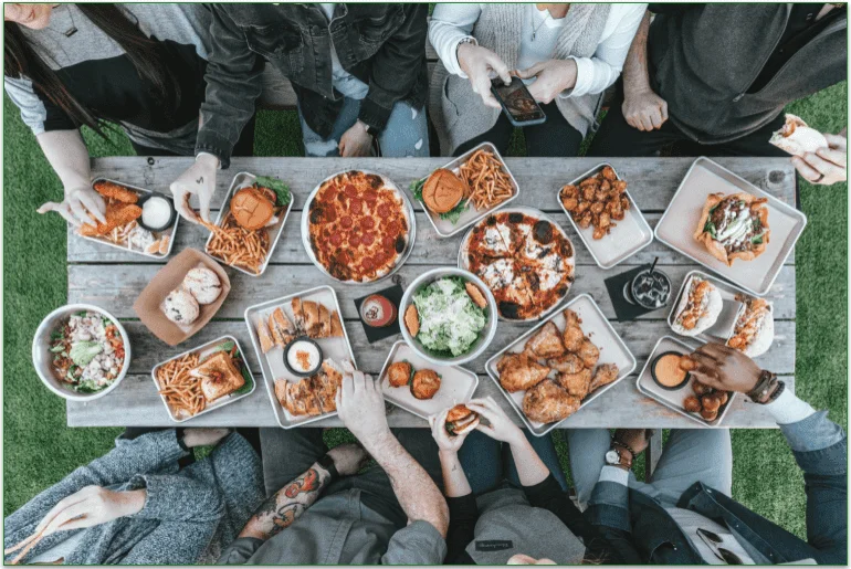 Table with plates of food and people sitting round it