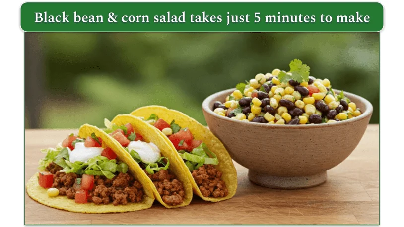 3 tacos beside a bowl of black bean and corn salad on a wooden table.