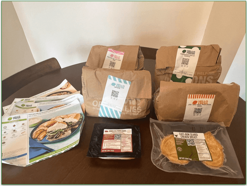 4 paper bags each containing ingredients for a HelloFresh recipe with recipe cards in front
