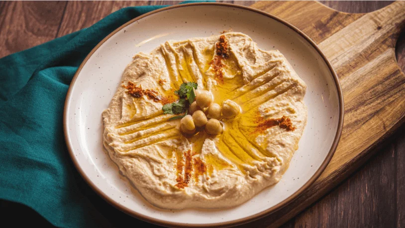 A plate of hummus on a table beside a teal tablecloth.