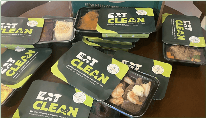 Photo of Eat Clean meals grouped on a table with cardboard packaging sleeves open to reveal the meals in microwaveable trays