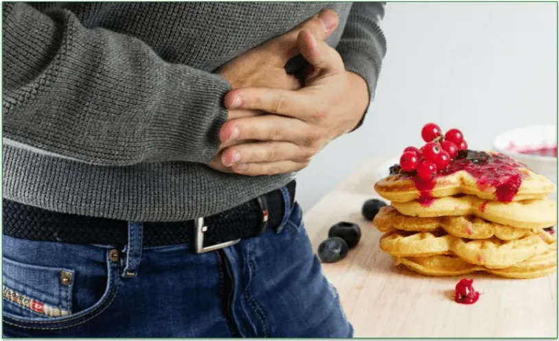 Man clutching his stomach with a pile of pancakes in the background