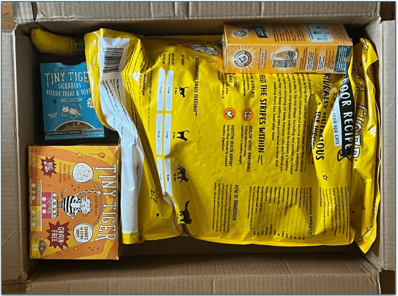 A ginger cat sits next to an open Chewy delivery