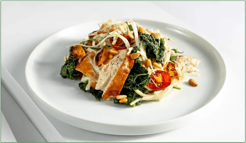 A plate of roasted chicken atop sliced vegetables with pine nuts.