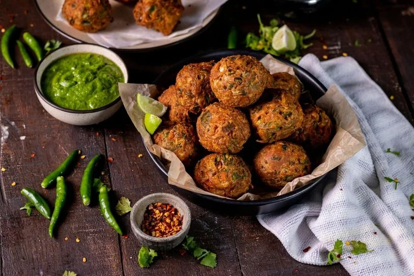 Meatballs stacked on a plate, next to a green dip