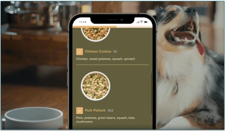  A phone open to the Nom Nom website with a dog in the background