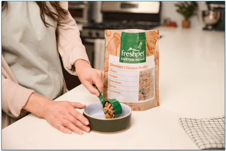 a person serving Freshpet into a bowl using a scoop