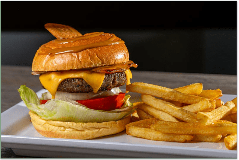 a burger with cheese on a bun with lettuce and tomato on plate with fries