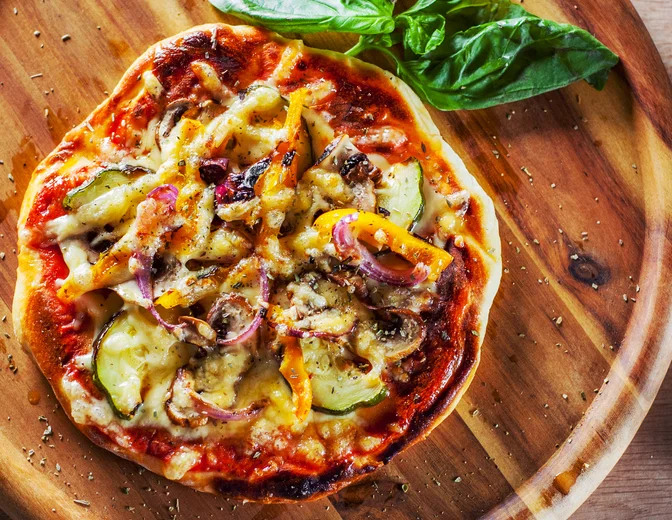 Pizza topped with zucchini, peppers, and red onion on a serving platter