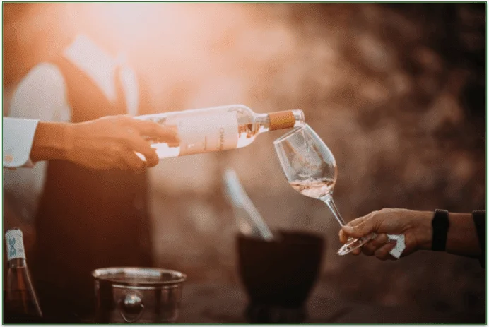 A man's hand pouring a glass of white wine into another man's glass.