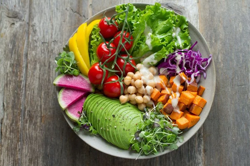 A salad with a variety of raw vegetables including chickpeas, avocado, and microgreens