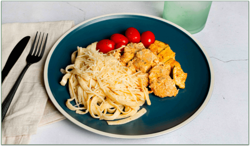 A plate of fettucini and chicken breast with cherry tomatoes.