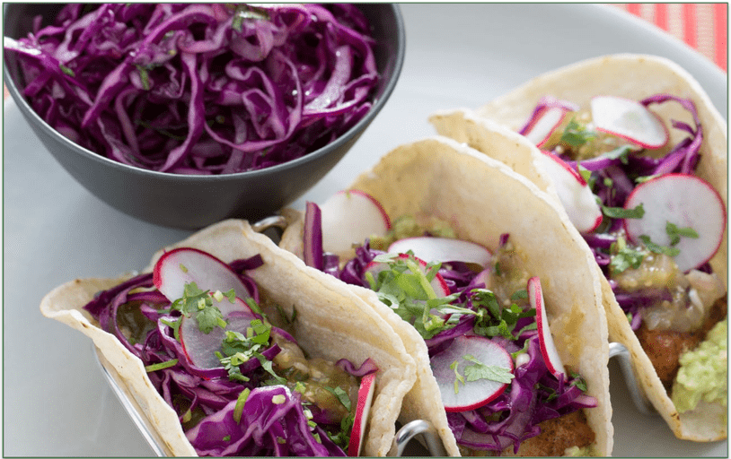 A bowl of purple cabbage slaw next to some tacos