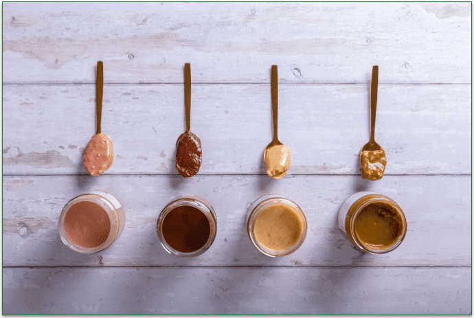 4 types of nut butters in a row with spoons on a table.