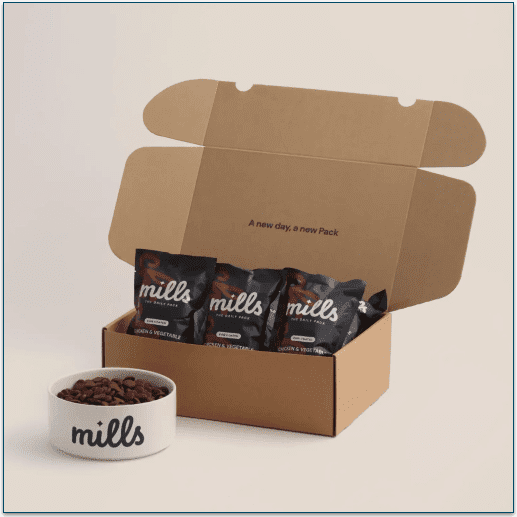 Picture of an open cardboard box containing Mills Daily Packs next to a dog food bowl