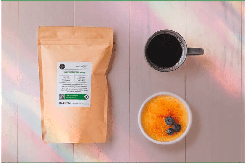 A bag of Dark Side of the Moon coffee with a creme brulee and a cup of coffee beside it.