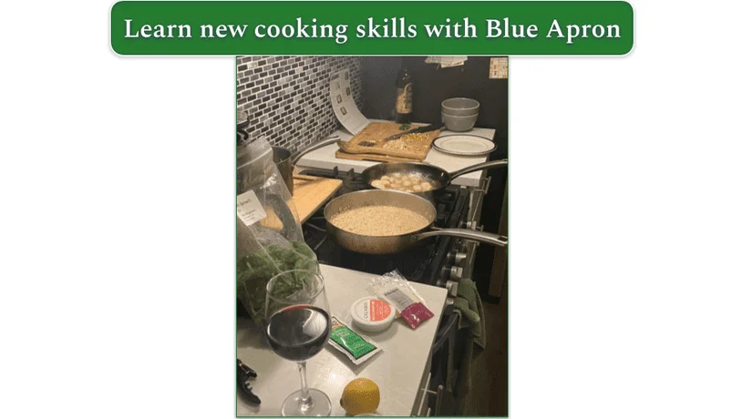 Two frying pans on a stove with a chopping board next to the stove and an open bag of greens