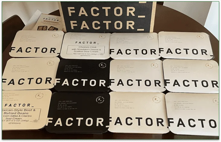 Photo of Factor's delivery box and 12 prepared meals stacked in front
