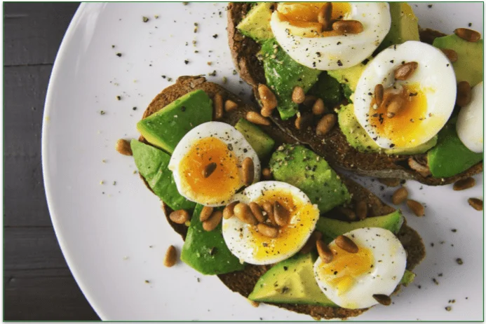 2 slices of toast on a plate with freshly sliced avocado, hard-boiled eggs, and hemp crunch.
