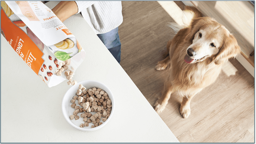 A freeze-dried meal being poured from a bag as a dog watches