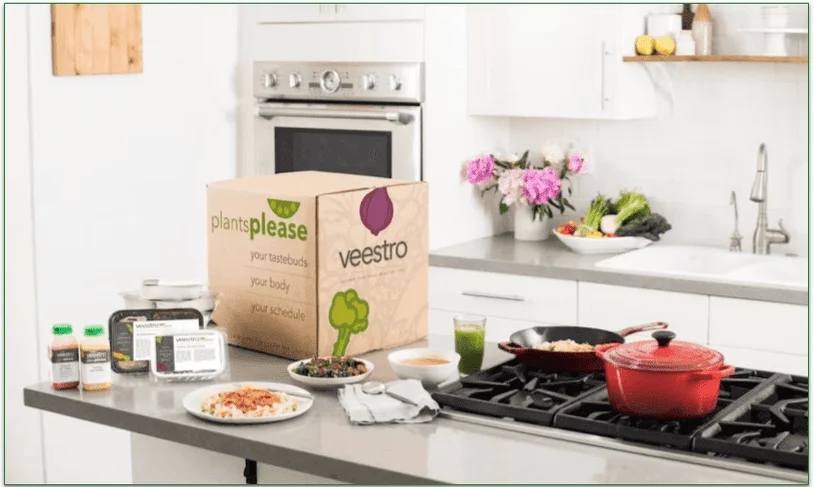 A Veestro delivery box on a counter next to plated meals and cooking pots