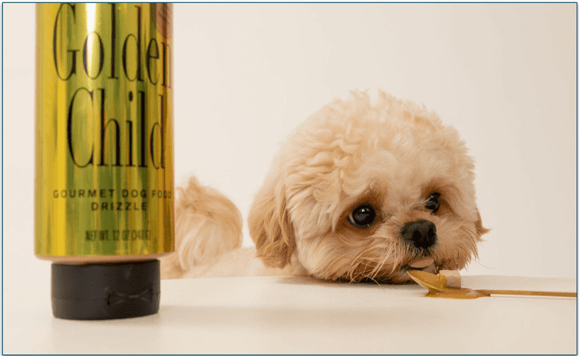 small fluffy dog licking a spoon next to a golden child drizzle bottle