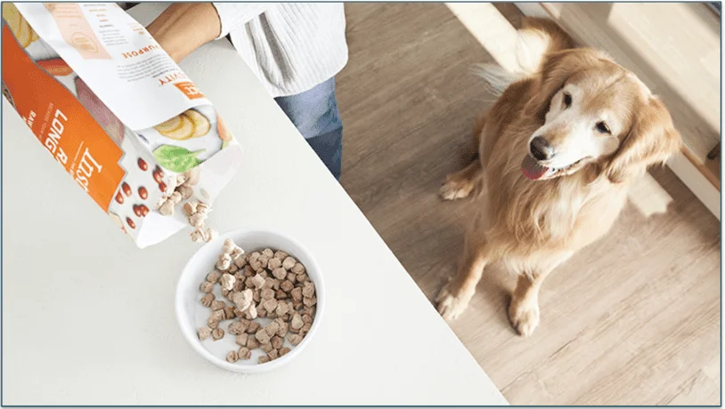 A freeze-dried meal being poured from a bag as a dog watches