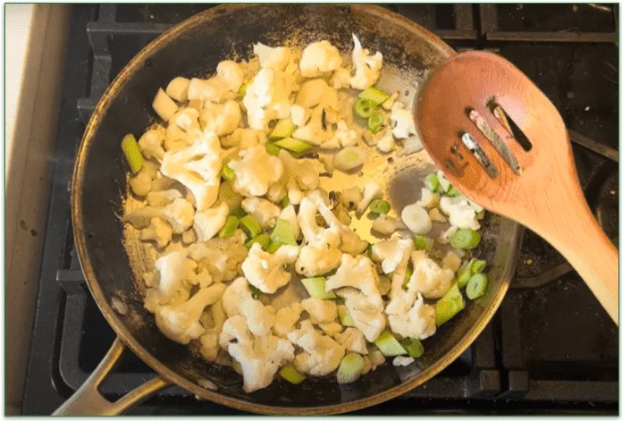 Photo of cauliflower florets and chopped leeks being stirred in a pan on the stove