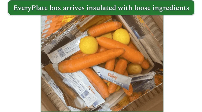 Image of an opened EveryPlate box with carrots, lemons, and sour cream squeeze packs.