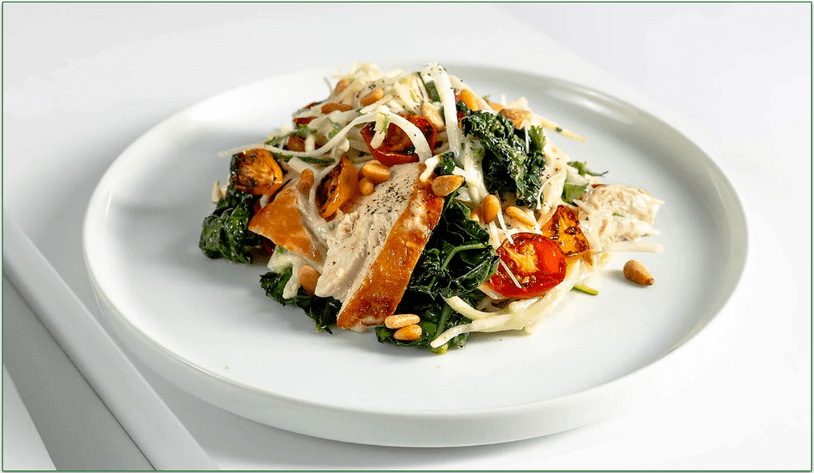 A plate of roasted chicken atop sliced vegetables with pine nuts.