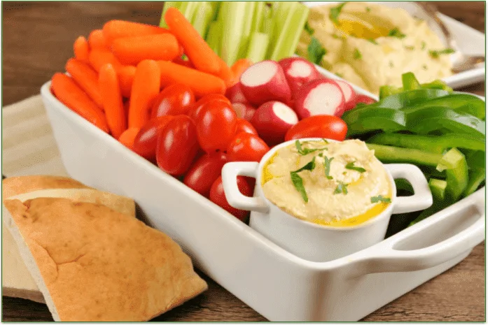 Some vegetables alongside some hummus and pita bread.