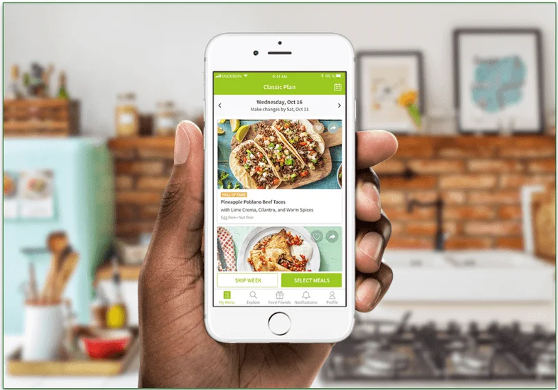 Image of a hand holding a mobile phone in a kitchen with HelloFresh's app on it