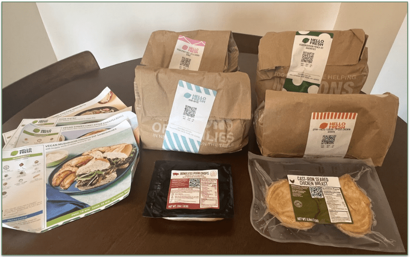 Photo of a HelloFresh delivery with 4 separate paper bags for each recipe, recipe cards, and separate proteins displayed on a table