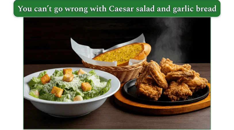 a bowl of caesar salad, a basket of garlic bread, and a plate of fried chicken on a wooden table